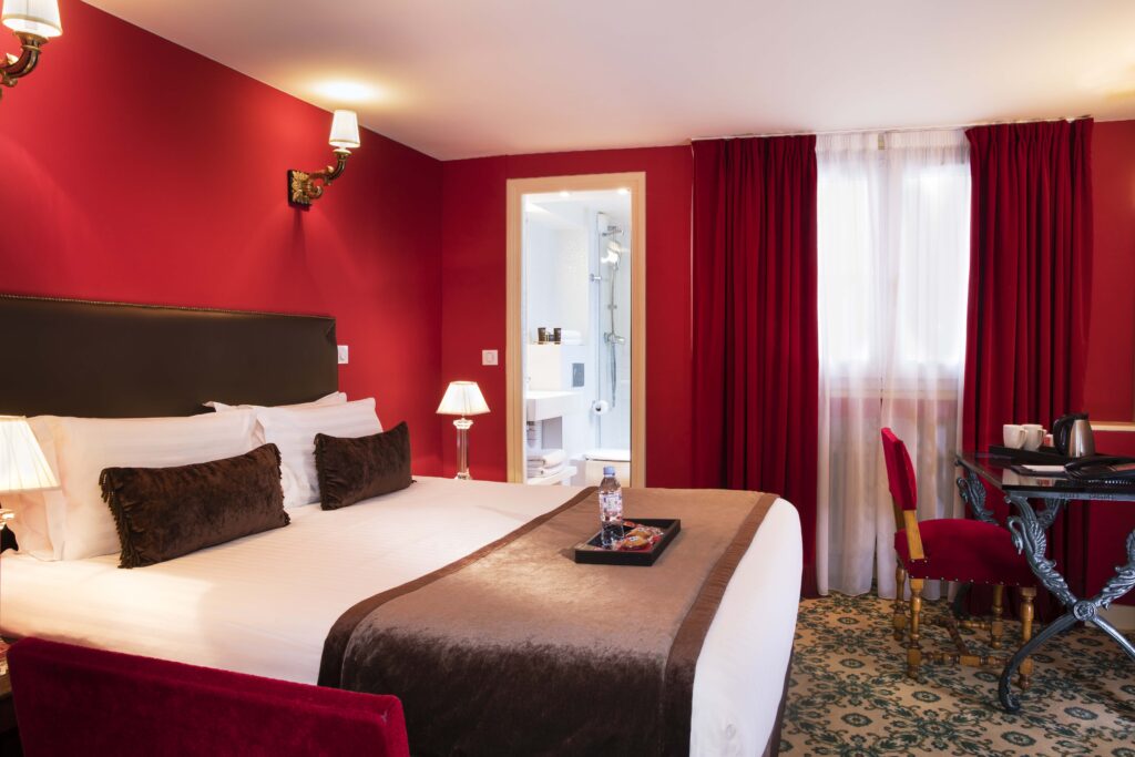 chambre avec tissus rouge, lit king size avec couvre lit et coussins marrons à l'hôtel des 2 continents à paris 6 - week-end en amoureux