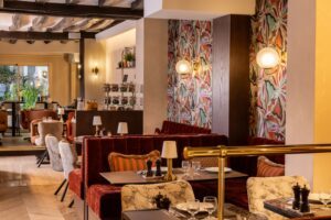 salle de petit-déjeuner avec tables dressées, salières et poivrières, lampes sur les tables, tissus fleuris, banquettes rouges, et poutres au plafond | petit-déjeuner healthy paris hotel des 2 Continents