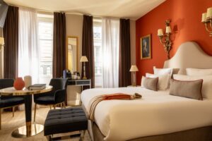 chambre avec manteau posé sur un lit blanc, fenêtres hautes et siège noir | soirée romantique à paris et à l'Hôtel des 2 Continents