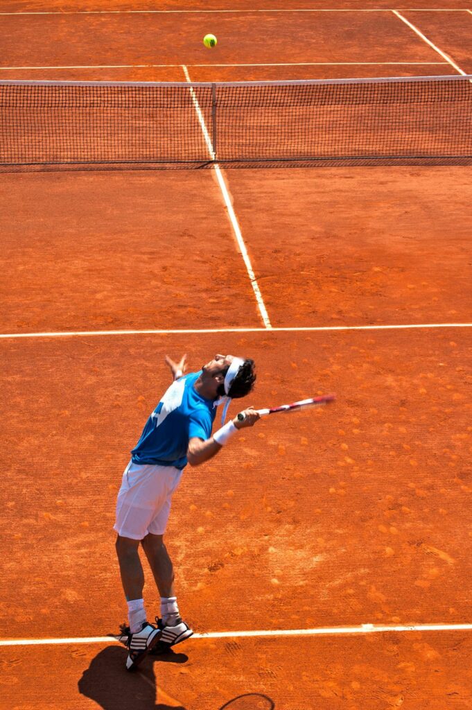 Hôtel Roland Garros Paris : Nous observons un joueur de tennis sur le point de frapper la balle envoyé par son adversaire. Le tout sur un terrain en terre battue, symbole du tournoi Roland Garros.